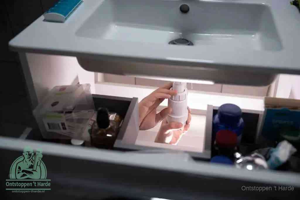 Een pompfles met zeep boven een wastafel, de heet water en afwasmiddel-methode om een vetprop in de afvoer los te maken in t Harde