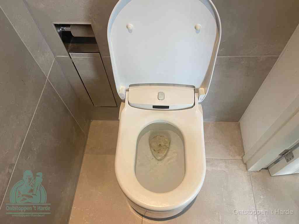 Een wit hangtoilet waarin een prop wc-papier op het water blijft drijven, een duidelijk signaal van een verstopte wc in t Harde