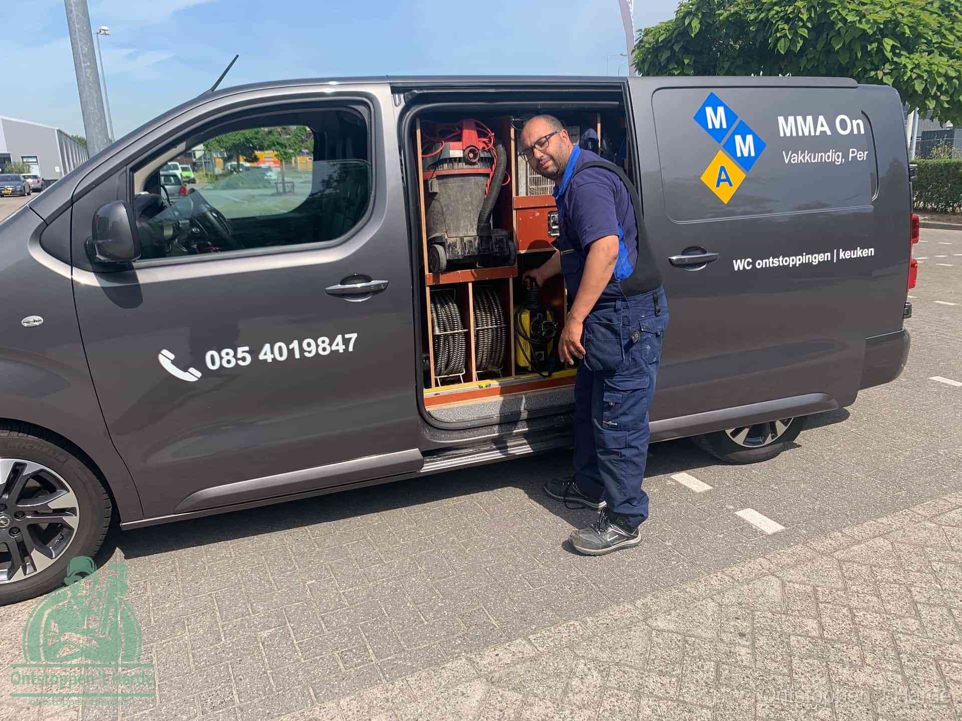 Een monteur bij de open schuifdeur van zijn bedrijfsbus op een parkeerplaats, klaar om de oorzaak van terugkerende afvoerverstoppingen aan te pakken in t Harde