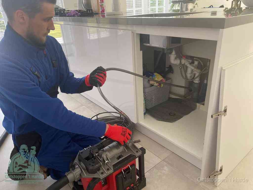 Een monteur reinigt de keukenafvoer grondig met een veermachine om terugkerende gootsteenverstoppingen te voorkomen in t Harde