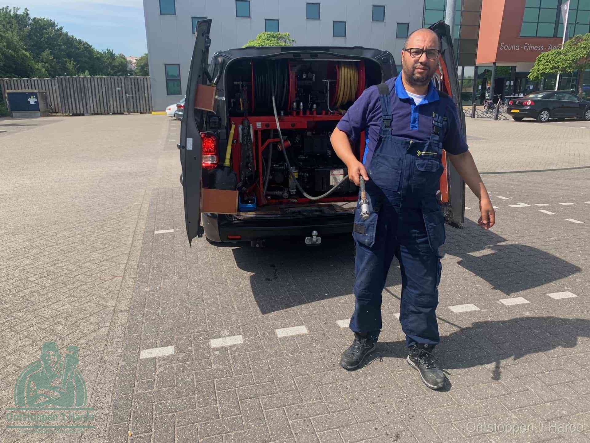 Een monteur bij zijn bestelbus met een hogedruk- en rioolreinigingsunit, klaar om de oorzaak van terugkerende wc-verstoppingen aan te pakken in t Harde